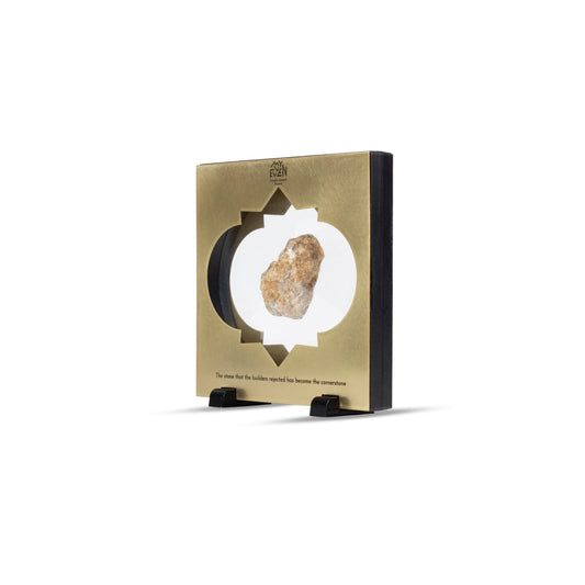 A side view of a natural stone suspended in the middle of a square bronze frame with a traditional middle eastern inlay that is set on two little black square stands. On the top of the frame is the "MyEvven" logo that says Temple Mount Stones below it. On the bottom of the frame, it reads "The stone that the builders rejected has become the cornerstone".