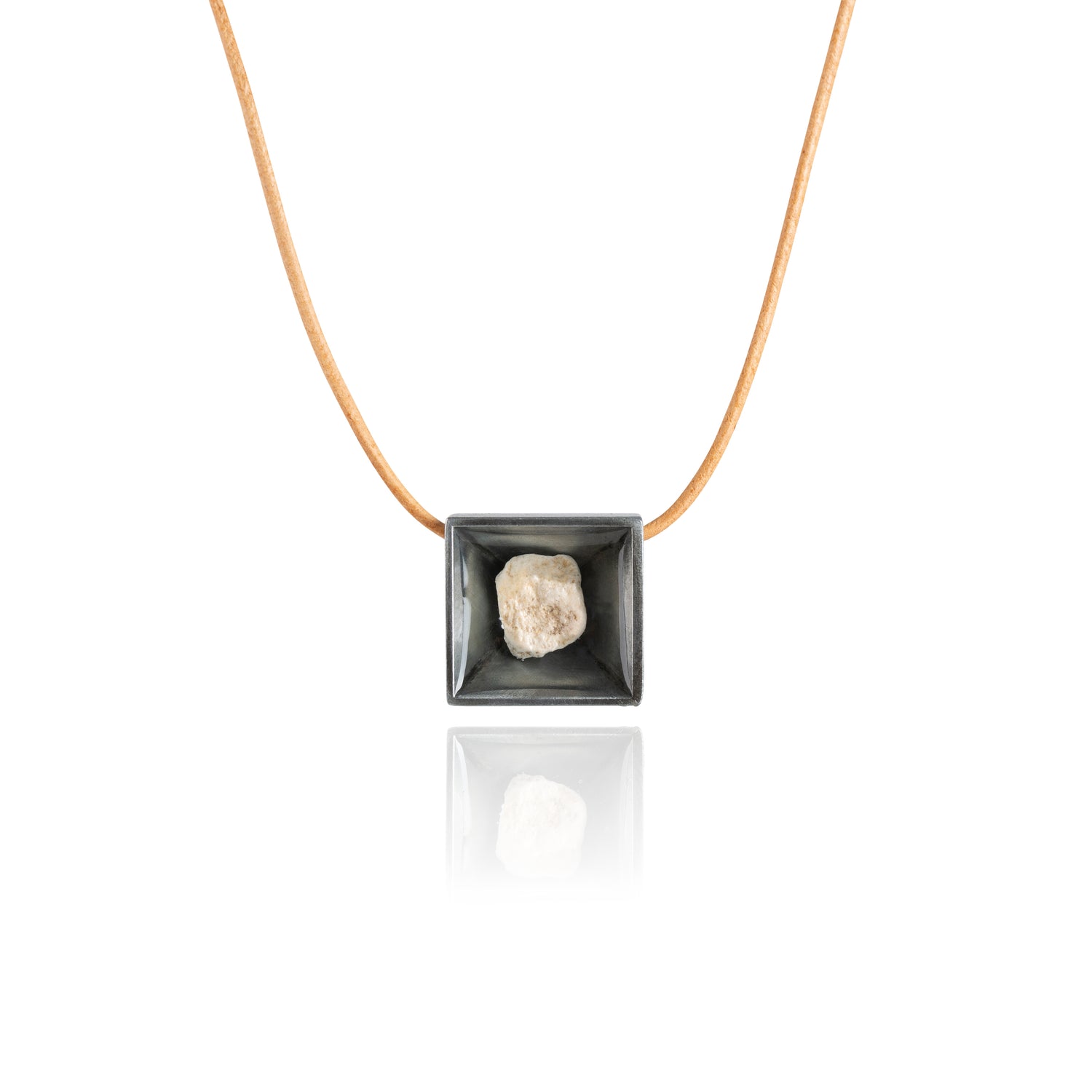 A small natural tan stone sitting in the middle of a square shaped metal pendant in a dark silver color. The pendant is hanging on a tan leather necklace.