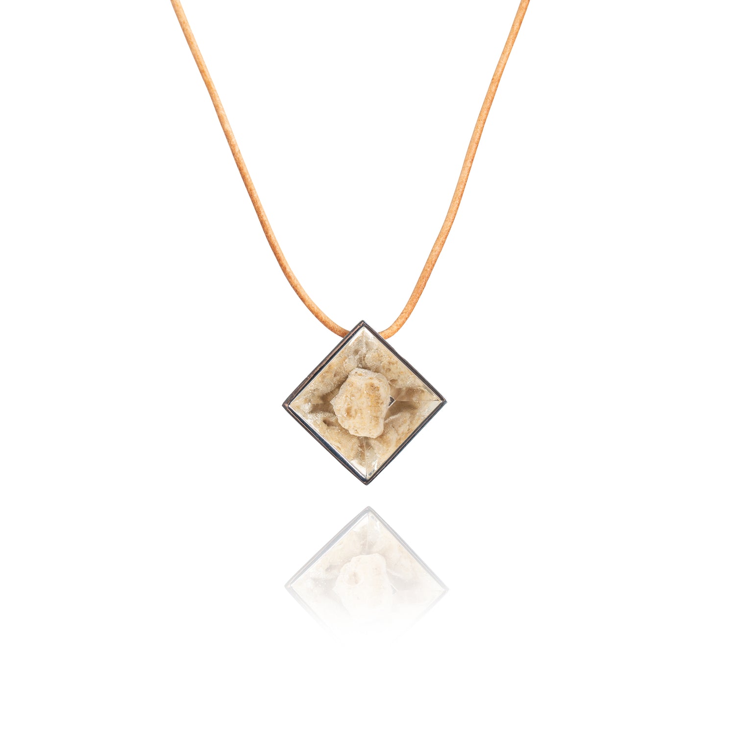 A small natural tan stone sitting in the middle of a diamond shaped metal pendant in a silver color. The pendant is hanging on a tan leather necklace.
