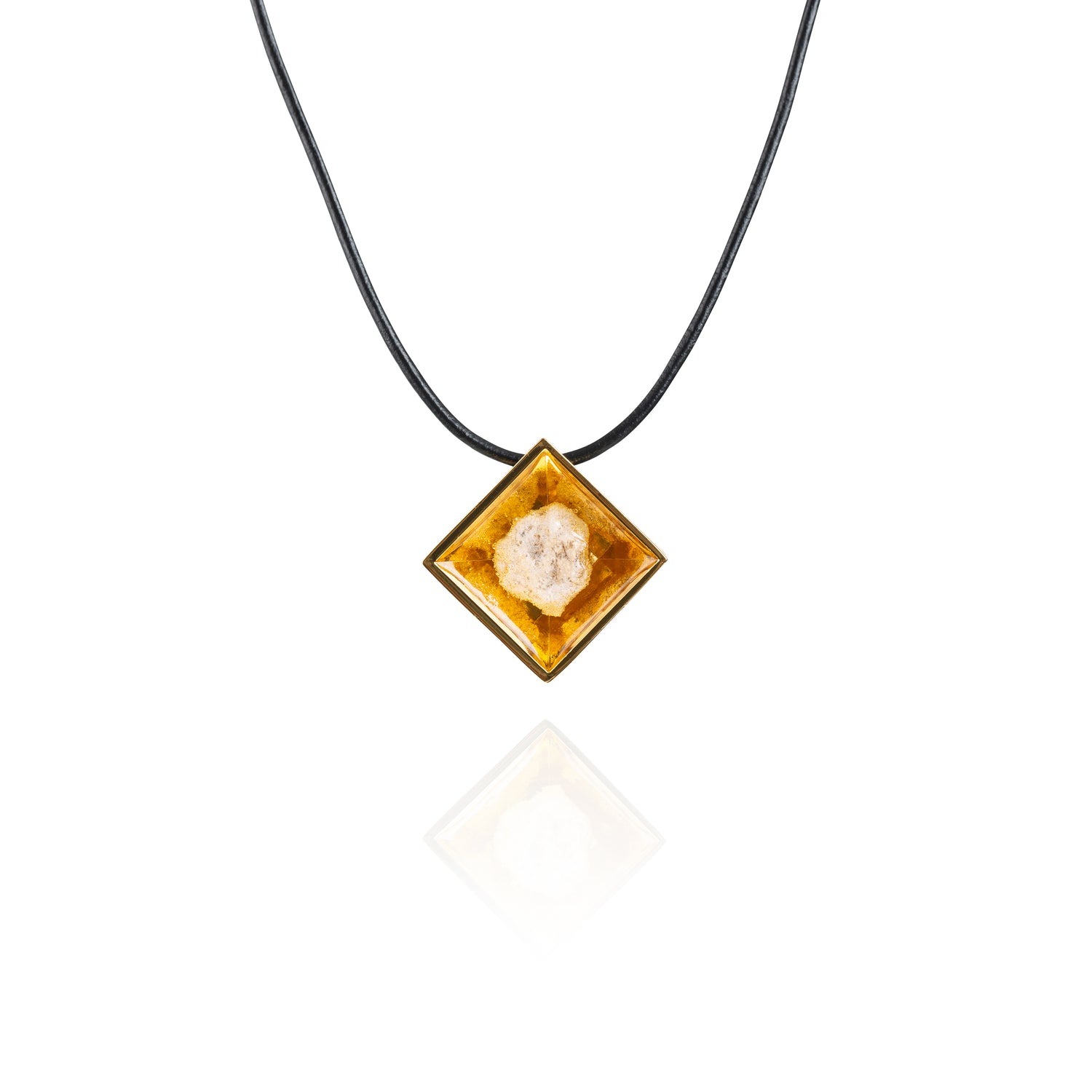 A small natural tan stone sitting in the middle of a diamond shaped metal pendant in a gold color. The pendant is hanging on a black leather necklace.