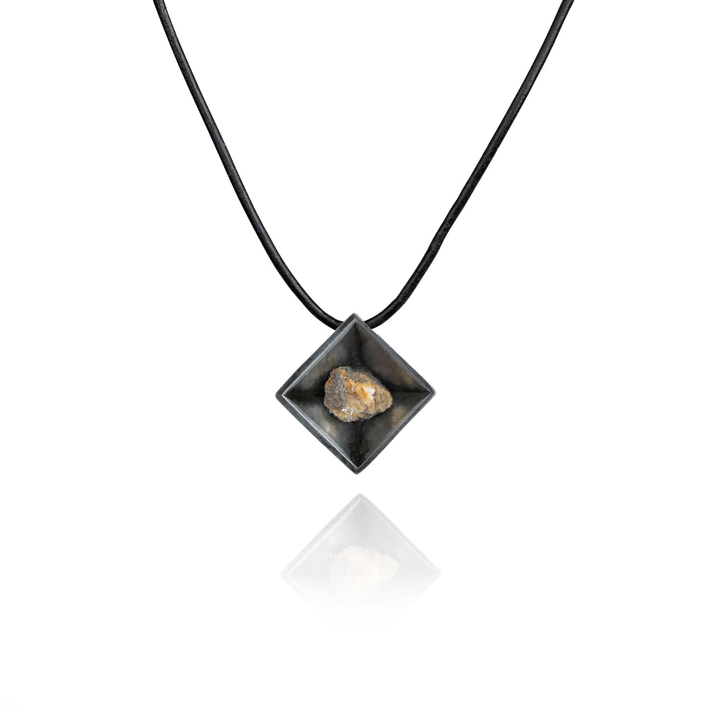 A small natural tan stone sitting in the middle of a diamond shaped metal pendant in a dark silver color. The pendant is hanging on a black leather necklace.