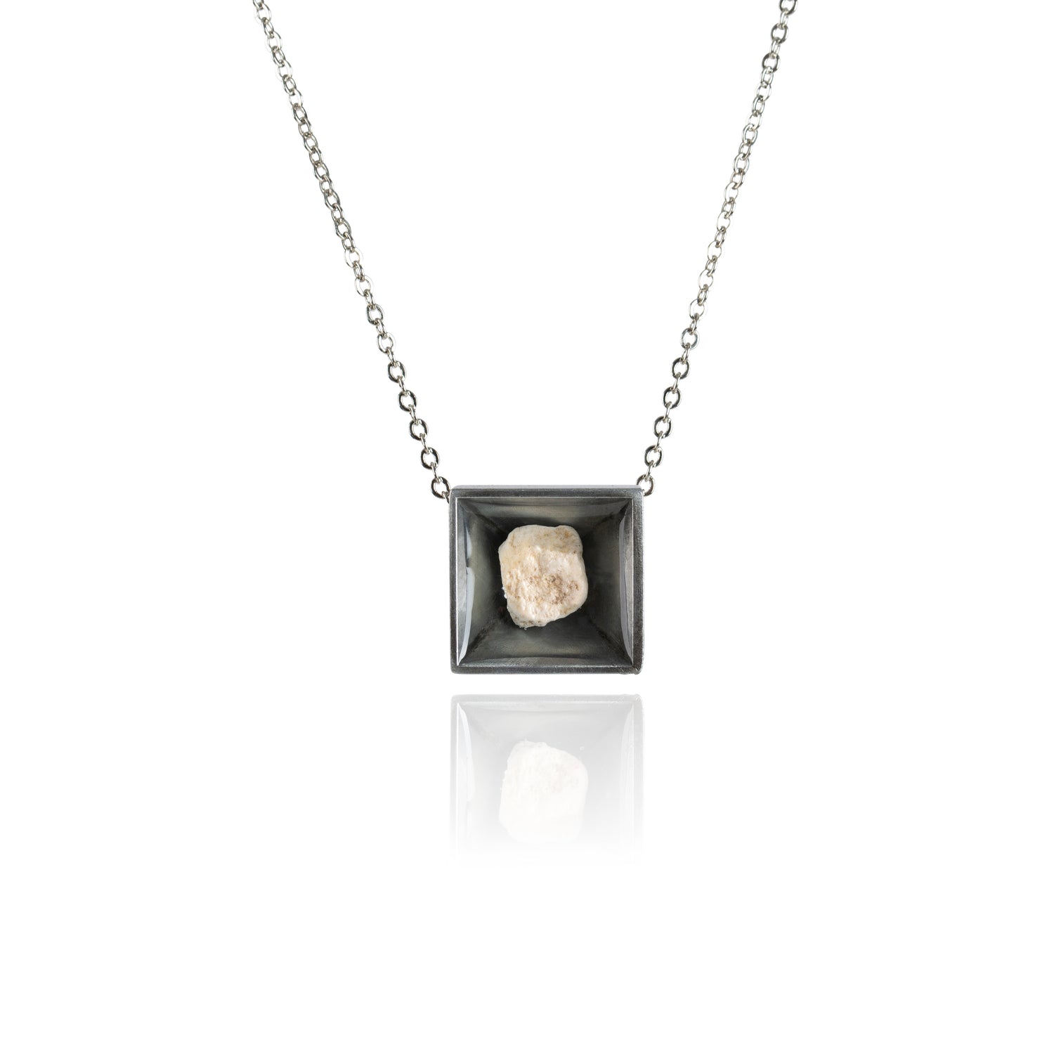 A small natural tan stone sitting in the middle of a square shaped metal pendant in a dark silver color. The pendant is hanging on a silver chain.