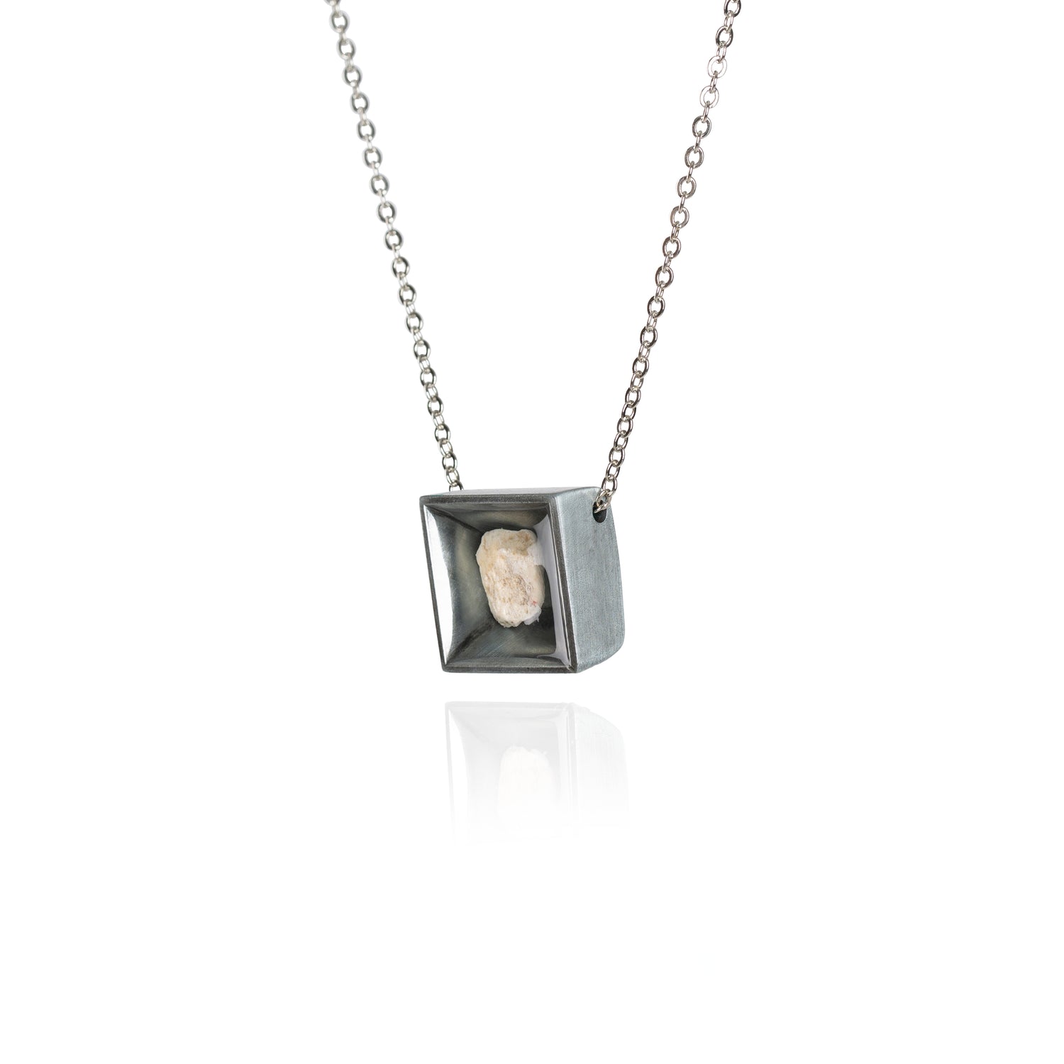 A side view of a small natural tan stone sitting in the middle of a square shaped metal pendant in a dark silver color. The pendant is hanging on a silver chain.
