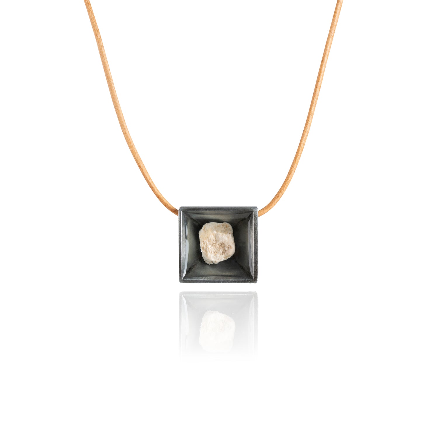 A small natural tan stone sitting in the middle of a square shaped metal pendant in a dark silver color. The pendant is hanging on a tan leather necklace.