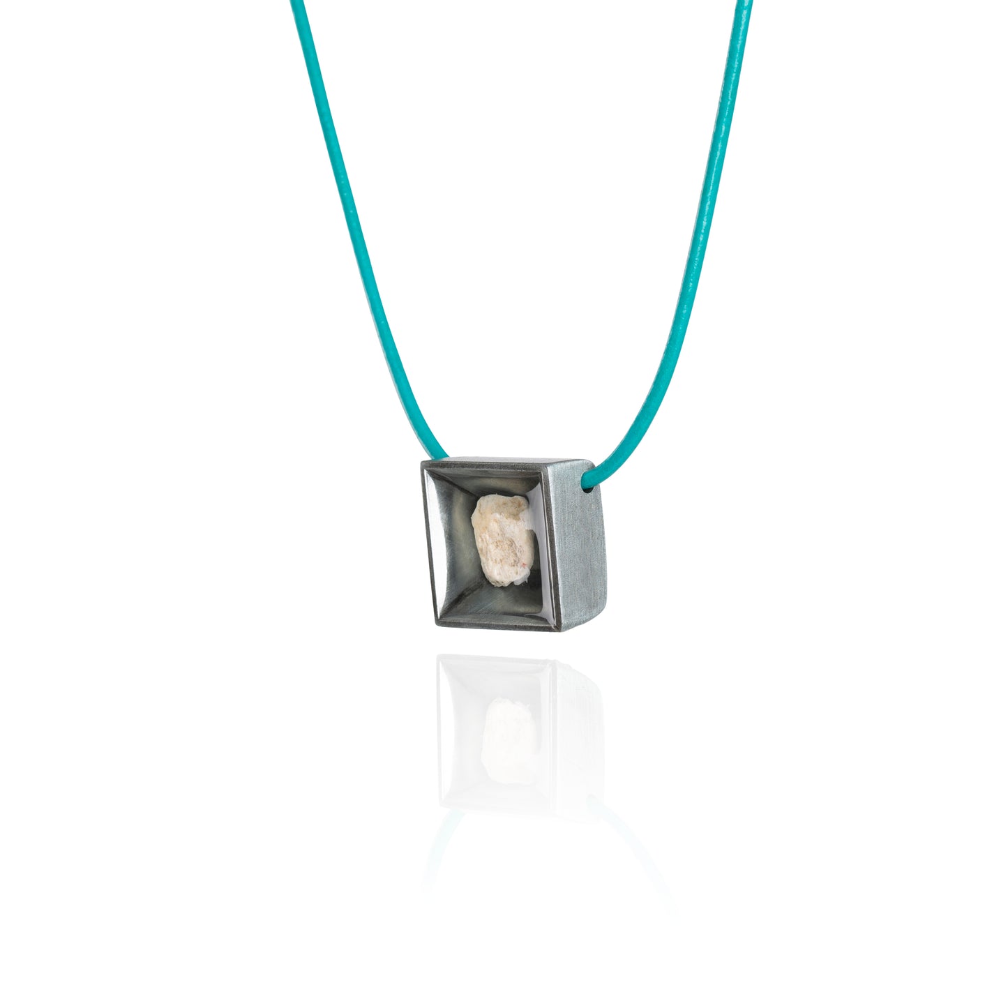 A side view of a small natural tan stone sitting in the middle of a square shaped metal pendant in a dark silver color. The pendant is hanging on a turquoise leather necklace.