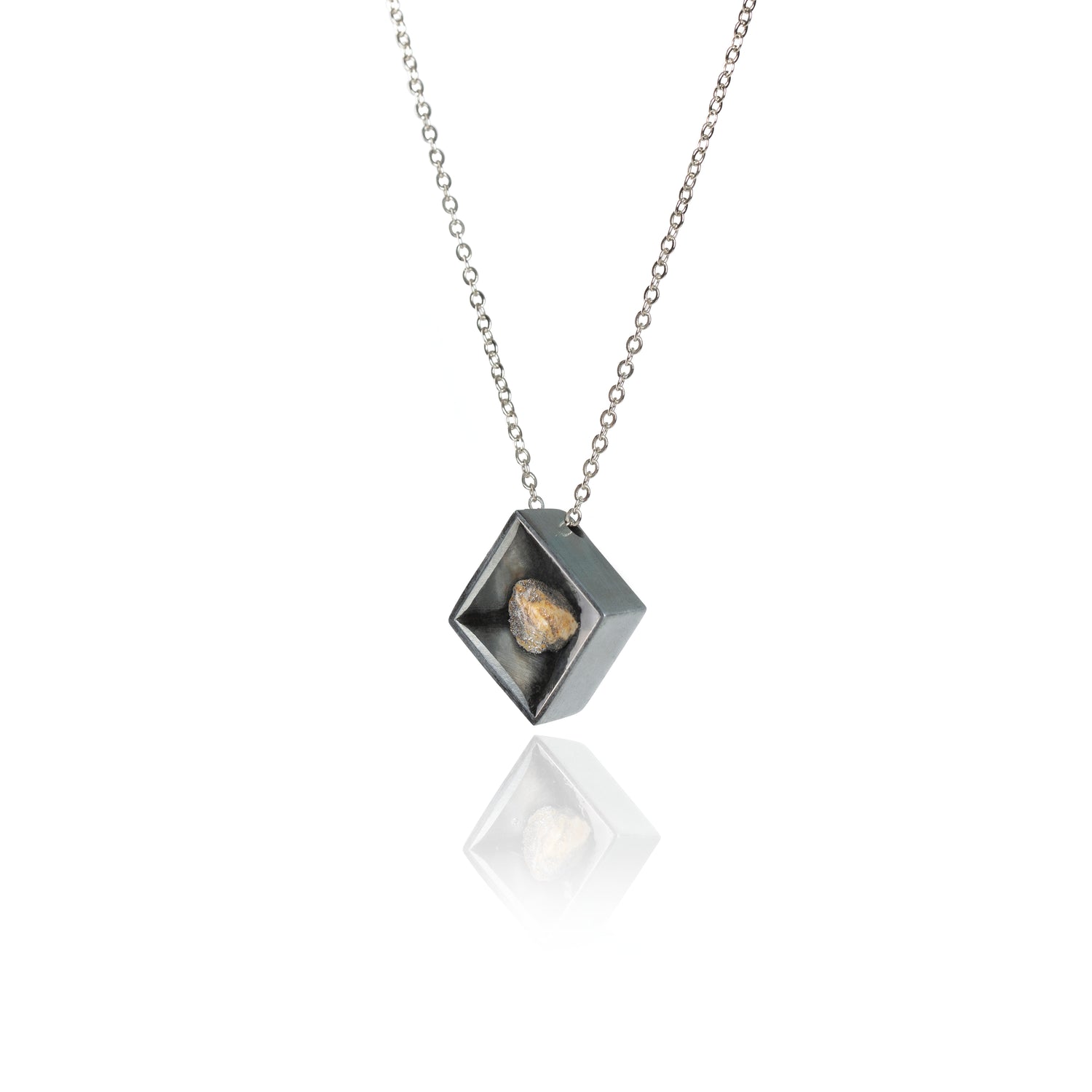 A side view of a small natural multicolored stone sitting in the middle of a diamond shaped metal pendant in a dark silver color. The pendant is hanging on silver chain.