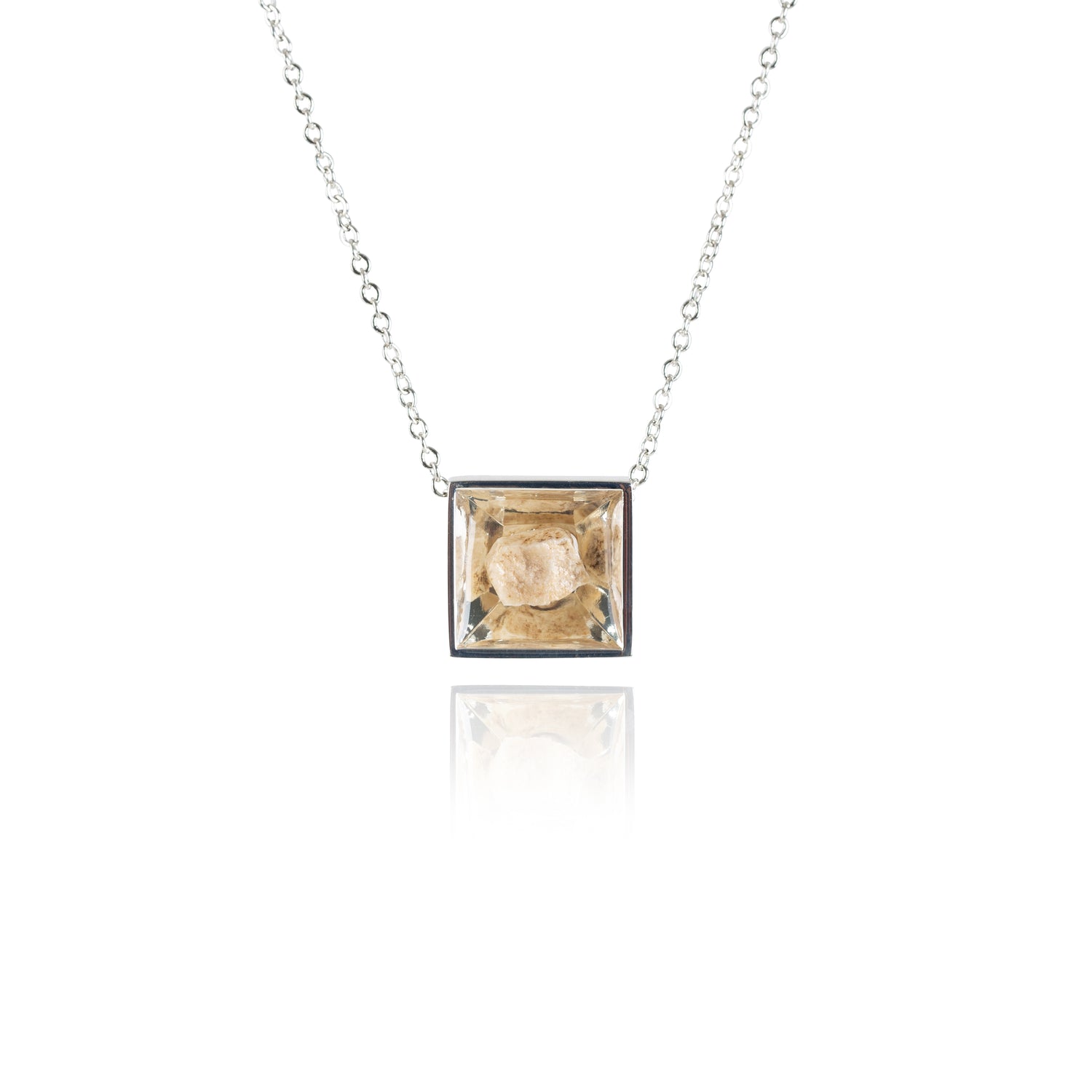 A small natural tan stone sitting in the middle of a square shaped metal pendant in a silver color. The pendant is hanging on a silver chain.