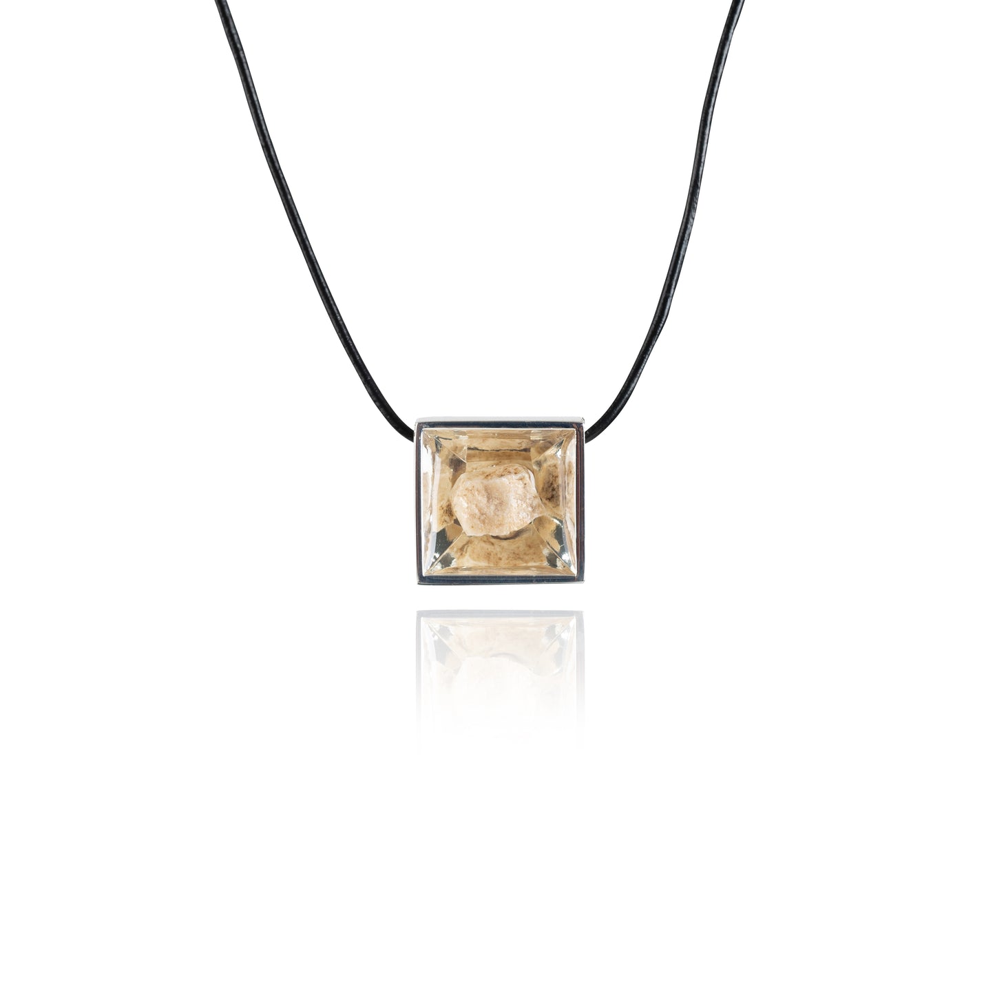 A small natural tan stone sitting in the middle of a square shaped metal pendant in a silver color. The pendant is hanging on a black leather necklace.