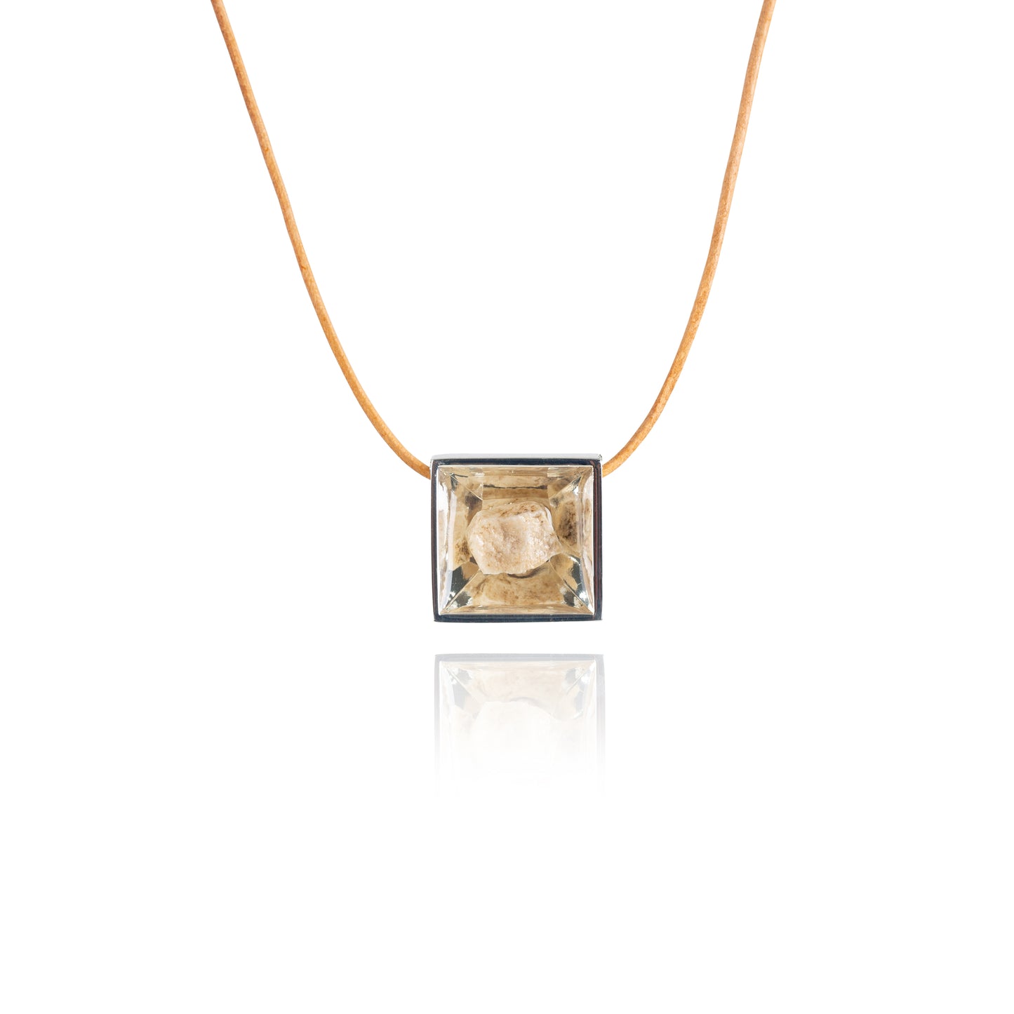 A small natural tan stone sitting in the middle of a square shaped metal pendant in a silver color. The pendant is hanging on a tan leather necklace.