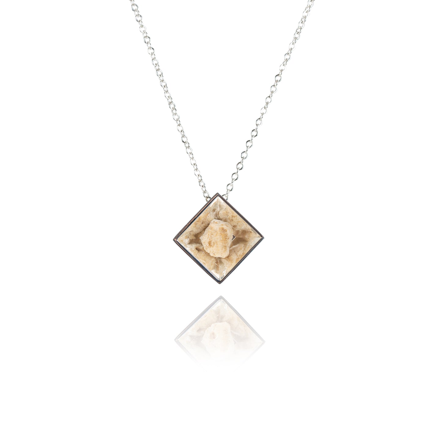 A small natural tan stone sitting in the middle of a diamond shaped metal pendant in a silver color. The pendant is hanging on silver chain.