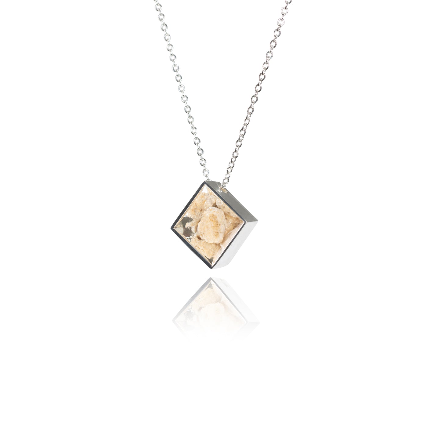 A side view of a small natural tan stone sitting in the middle of a diamond shaped metal pendant in a silver color on the outside and bright tan color on the inside. The pendant is hanging on silver chain.