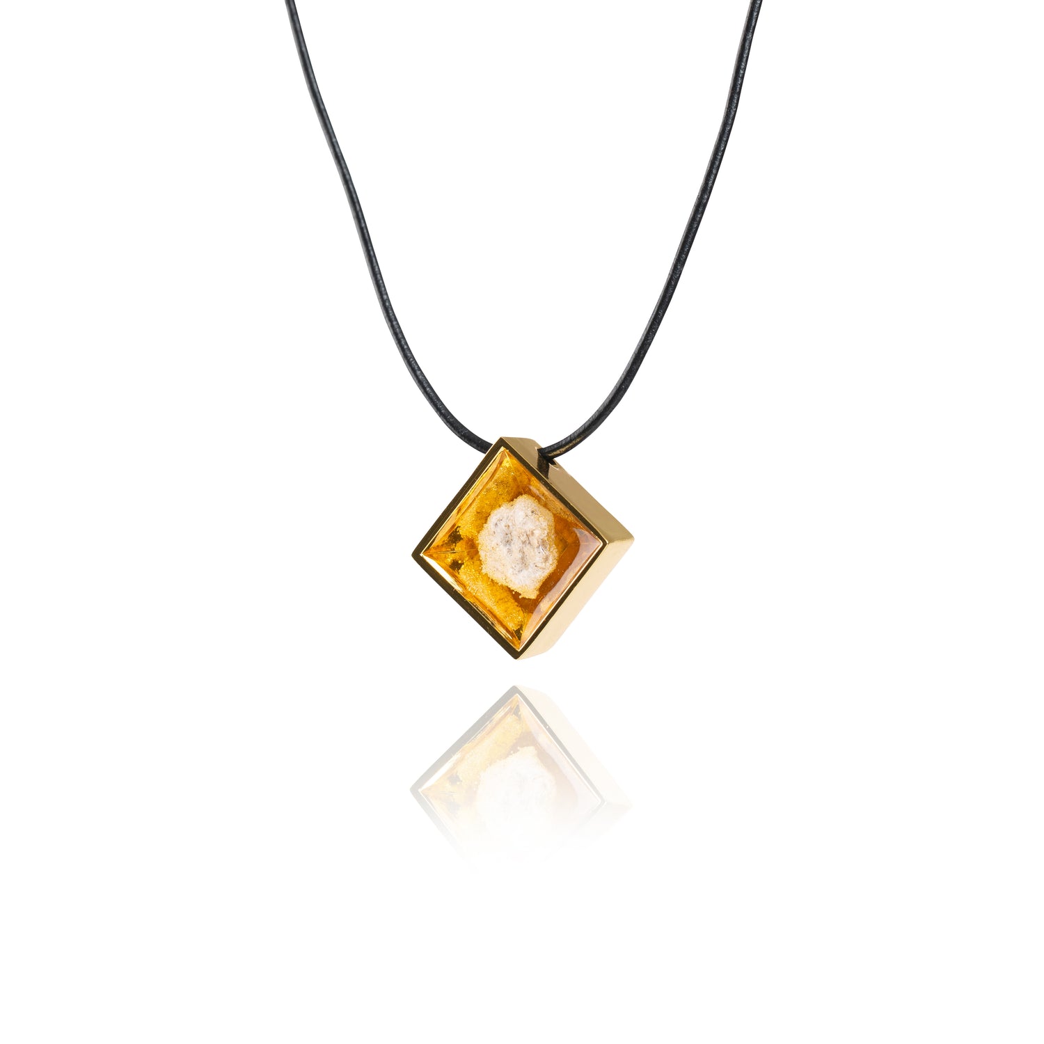 A side view of a small natural tan stone sitting in the middle of a diamond shaped metal pendant in a gold color. The pendant is hanging on a black leather necklace.