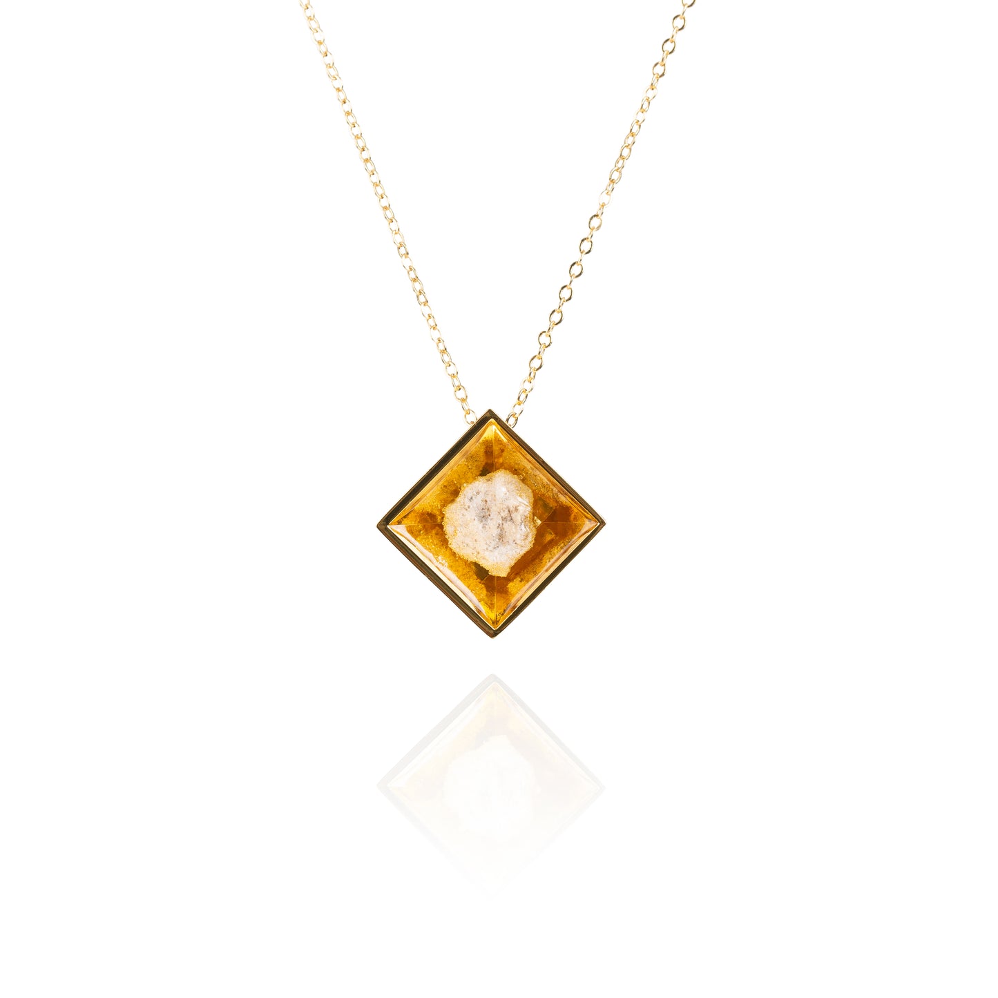 A small natural tan stone sitting in the middle of a diamond shaped metal pendant in a gold color. The pendant is hanging on a gold chain.