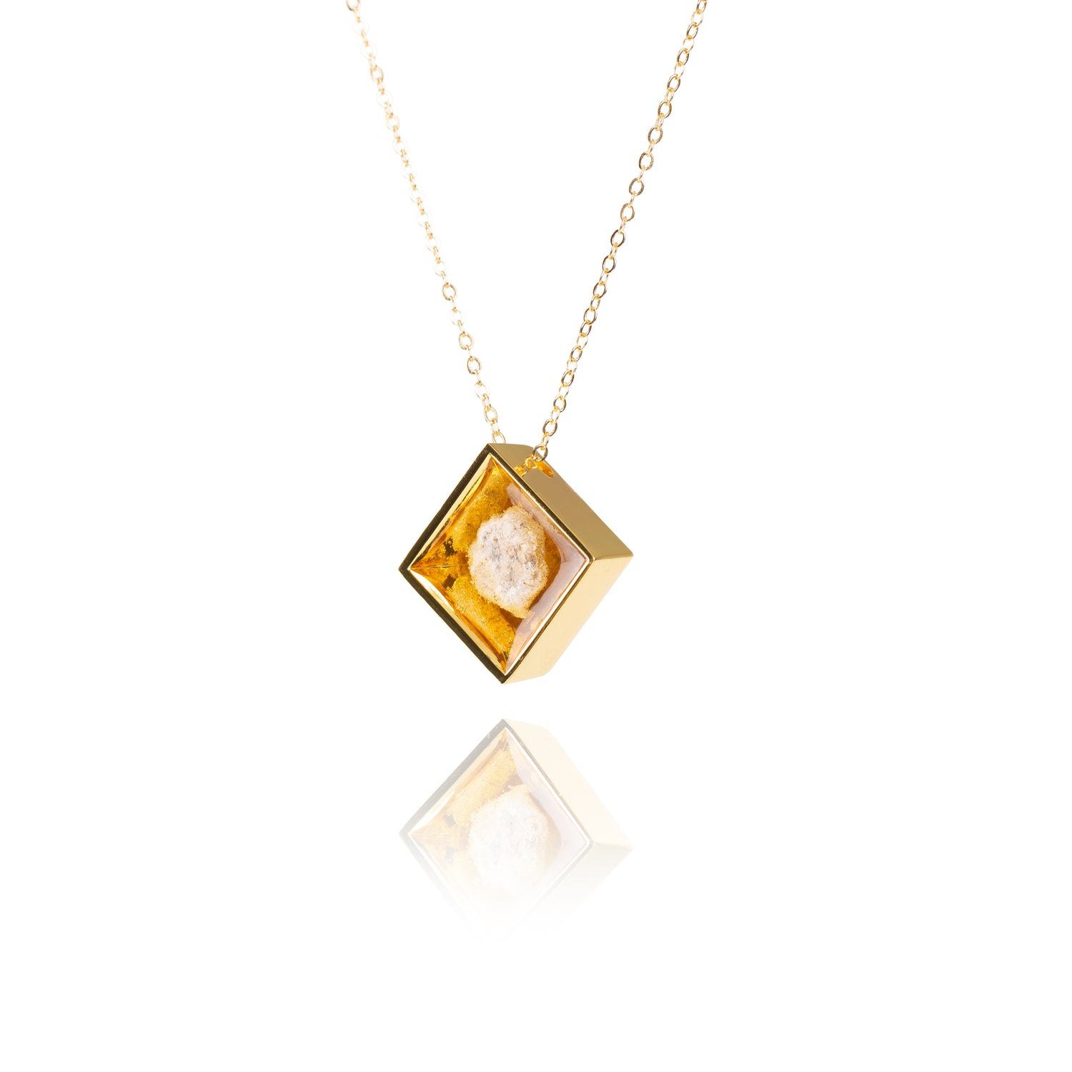 A side view of a small natural tan stone sitting in the middle of a diamond shaped metal pendant in a gold color. The pendant is hanging on a gold chain.