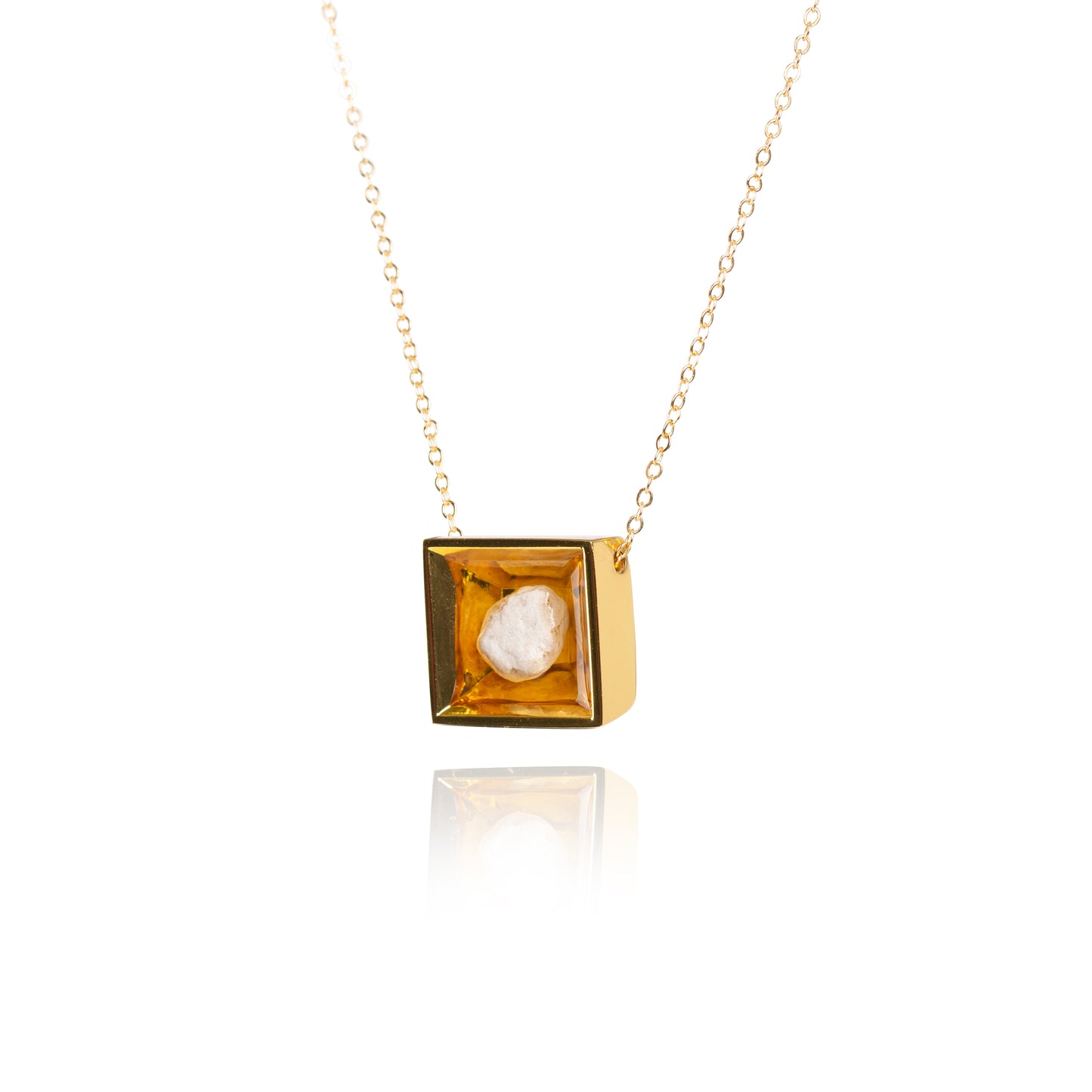 A side view of a small natural tan stone sitting in the middle of a square shaped metal pendant in a gold color. The pendant is hanging on a gold chain.