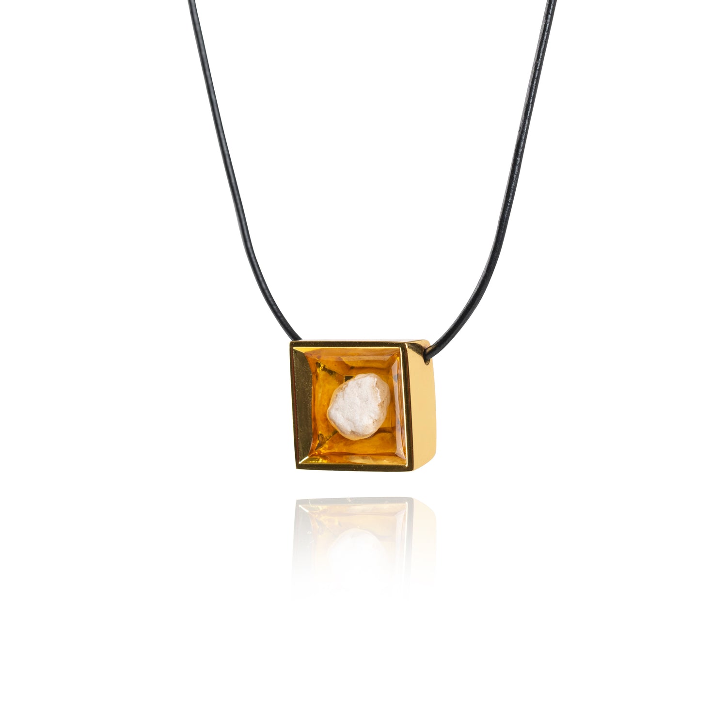 A side view of a small natural tan stone sitting in the middle of a square shaped metal pendant in a gold color. The pendant is hanging on a black leather necklace.
