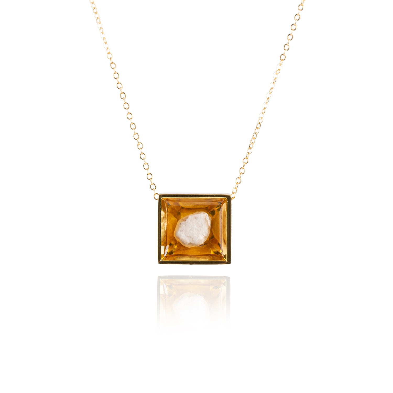 A small natural tan stone sitting in the middle of a square shaped metal pendant in a gold color. The pendant is hanging on a gold chain.