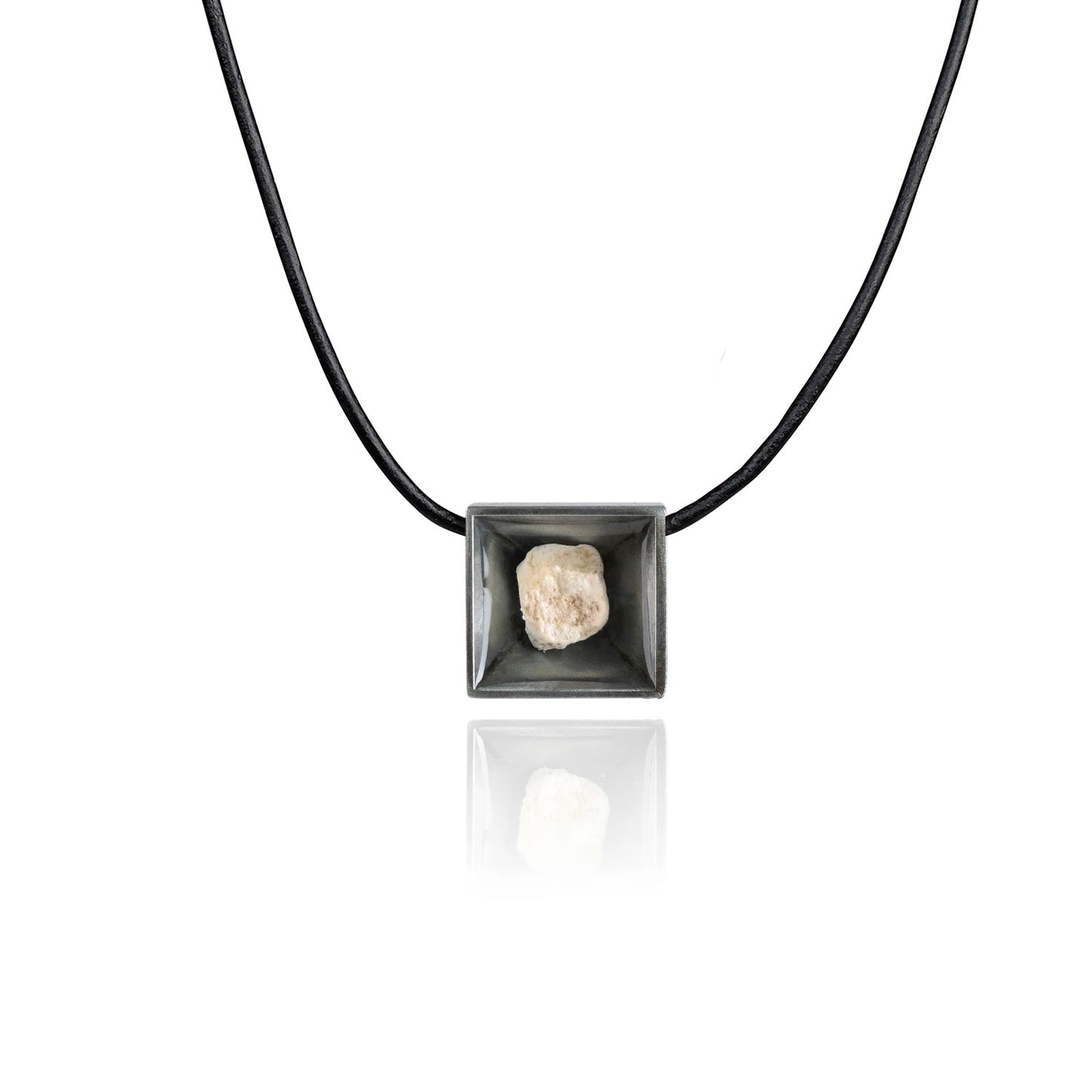 A small natural tan stone sitting in the middle of a square shaped metal pendant in a dark silver color. The pendant is hanging on a black leather necklace.