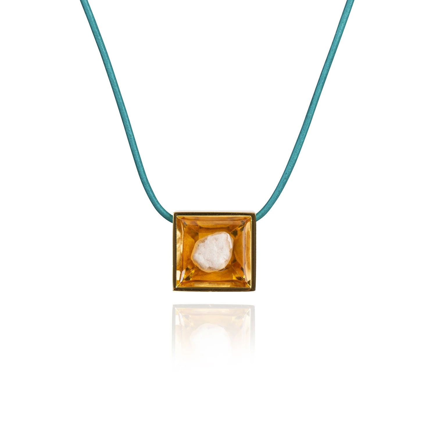 A small natural tan stone sitting in the middle of a square shaped metal pendant in a gold color. The pendant is hanging on a turquoise leather necklace.