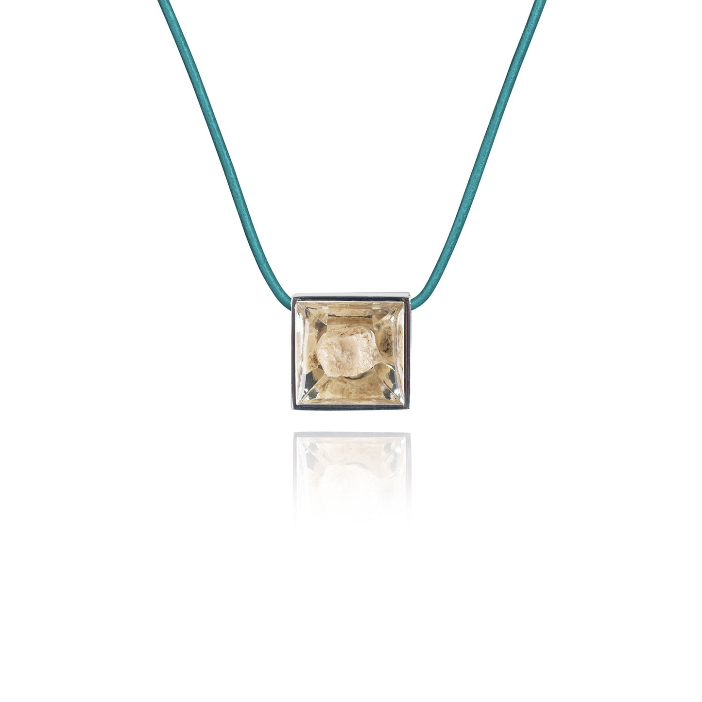 A small natural tan stone sitting in the middle of a square shaped metal pendant in a silver color. The pendant is hanging on a turquoise leather necklace.
