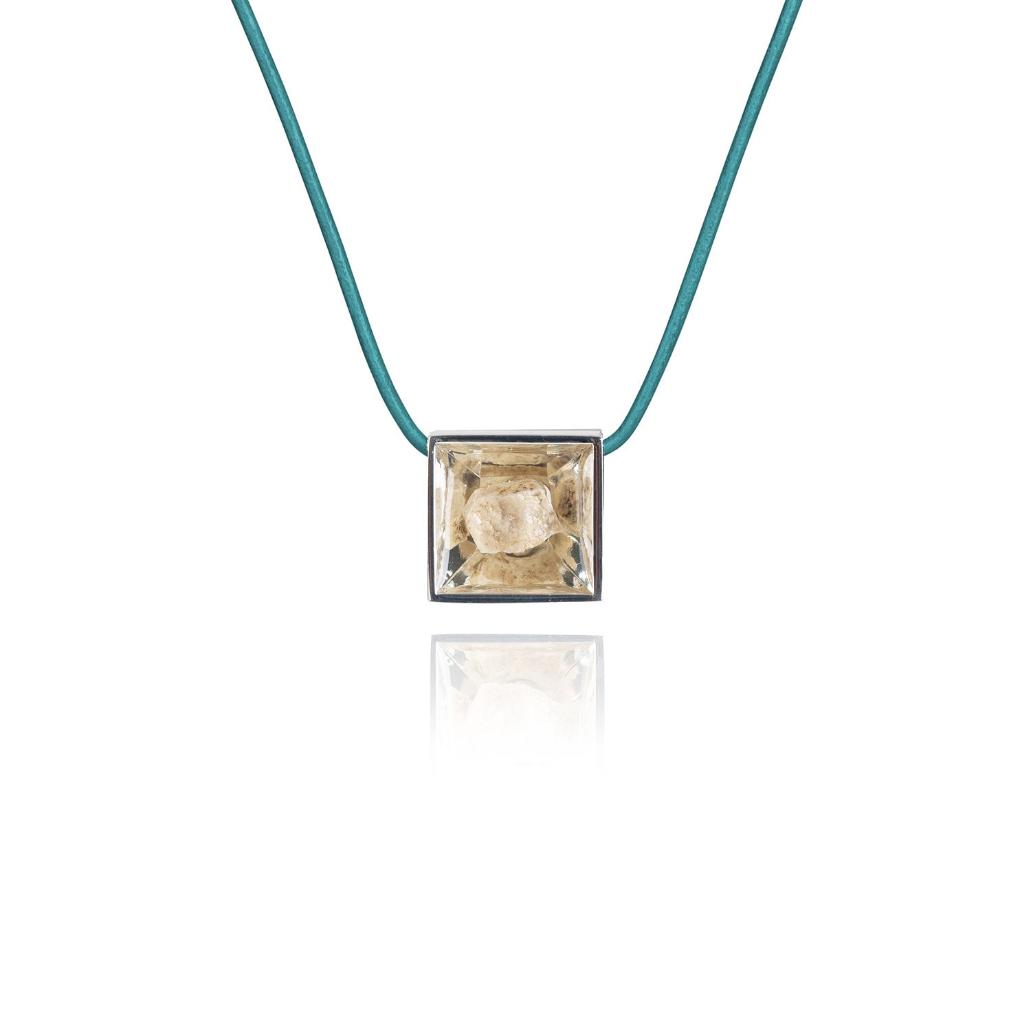 A small natural tan stone sitting in the middle of a square shaped metal pendant in a silver color. The pendant is hanging on a turquoise leather necklace.