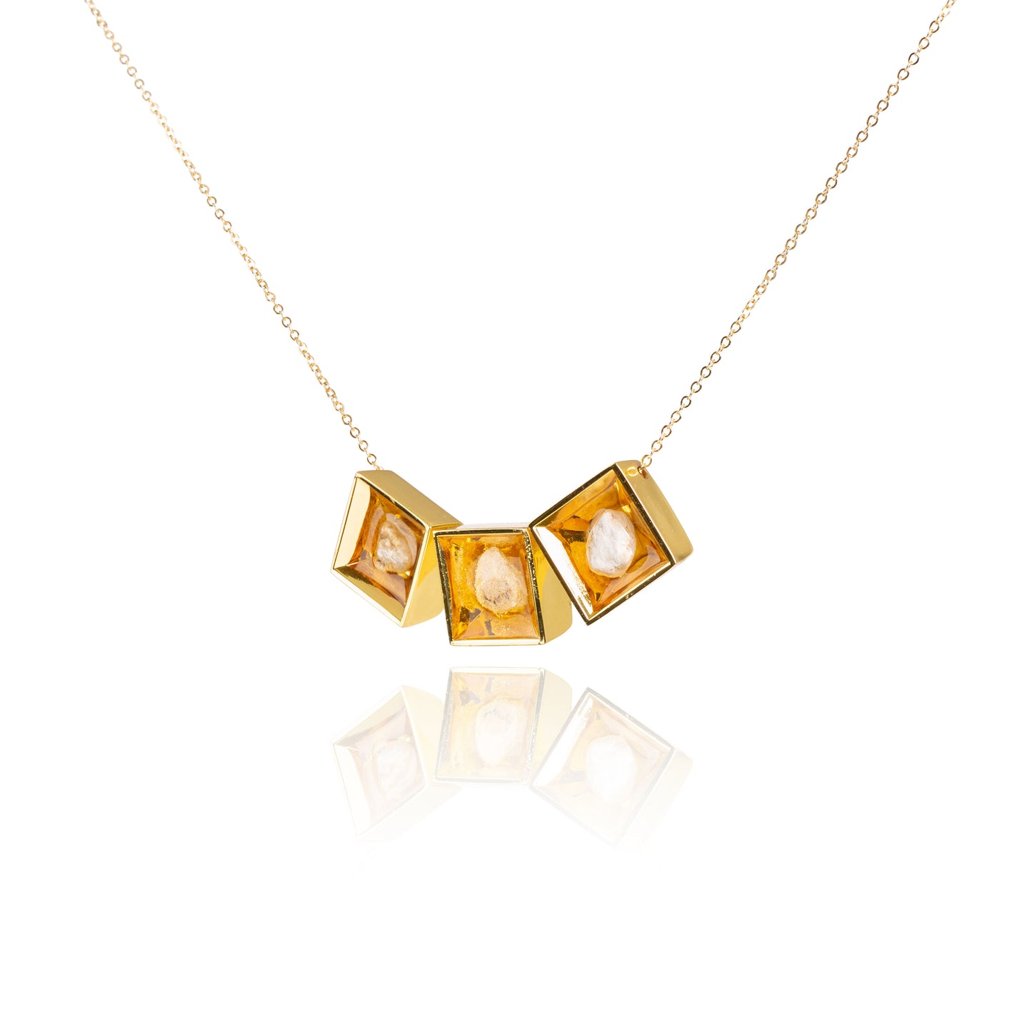 A side view of three small natural tan stones sitting in the middle of three separate square shaped metal pendants in a gold color. The pendants are hanging on a gold chain.