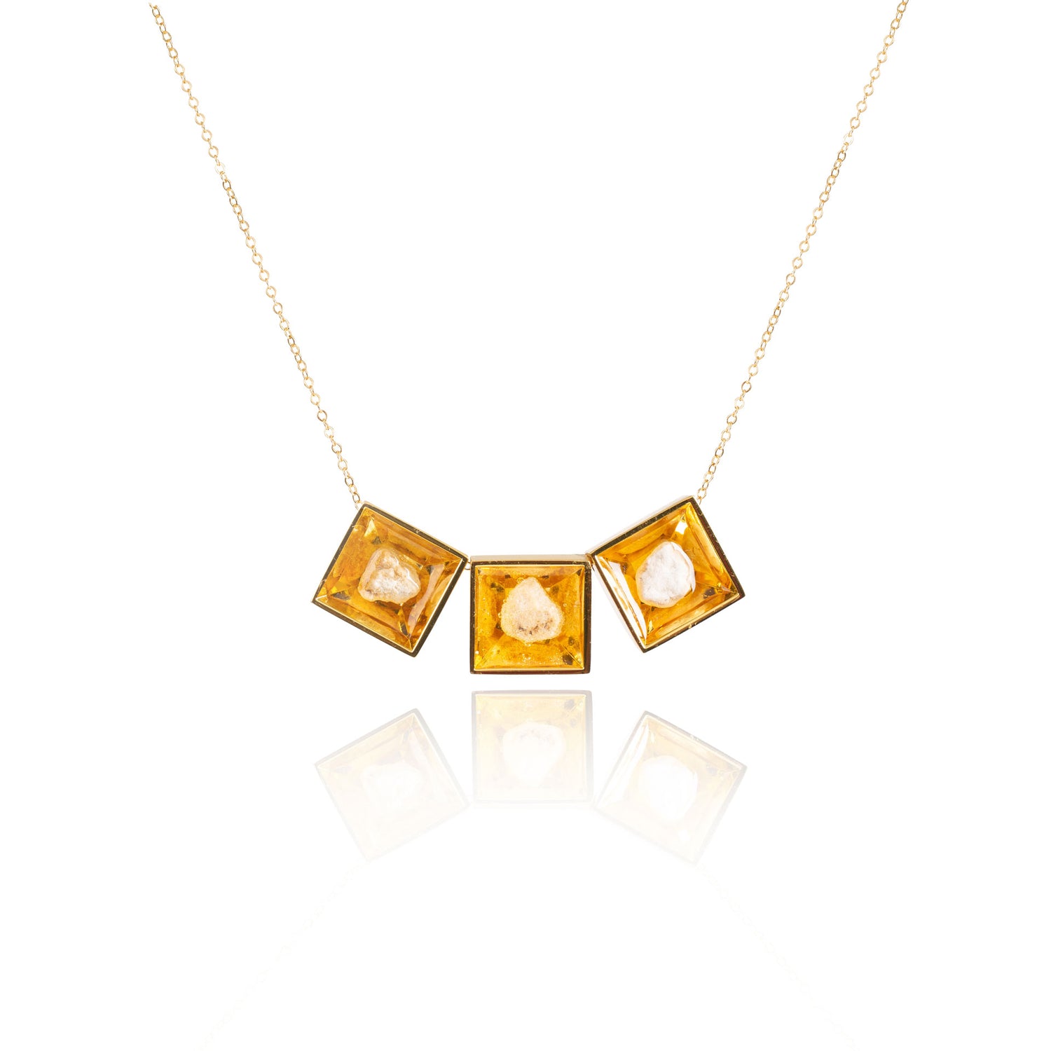 Three small natural tan stones sit in the middle of three separate square shaped metal pendants in a gold color. The pendants are hanging on a gold chain.