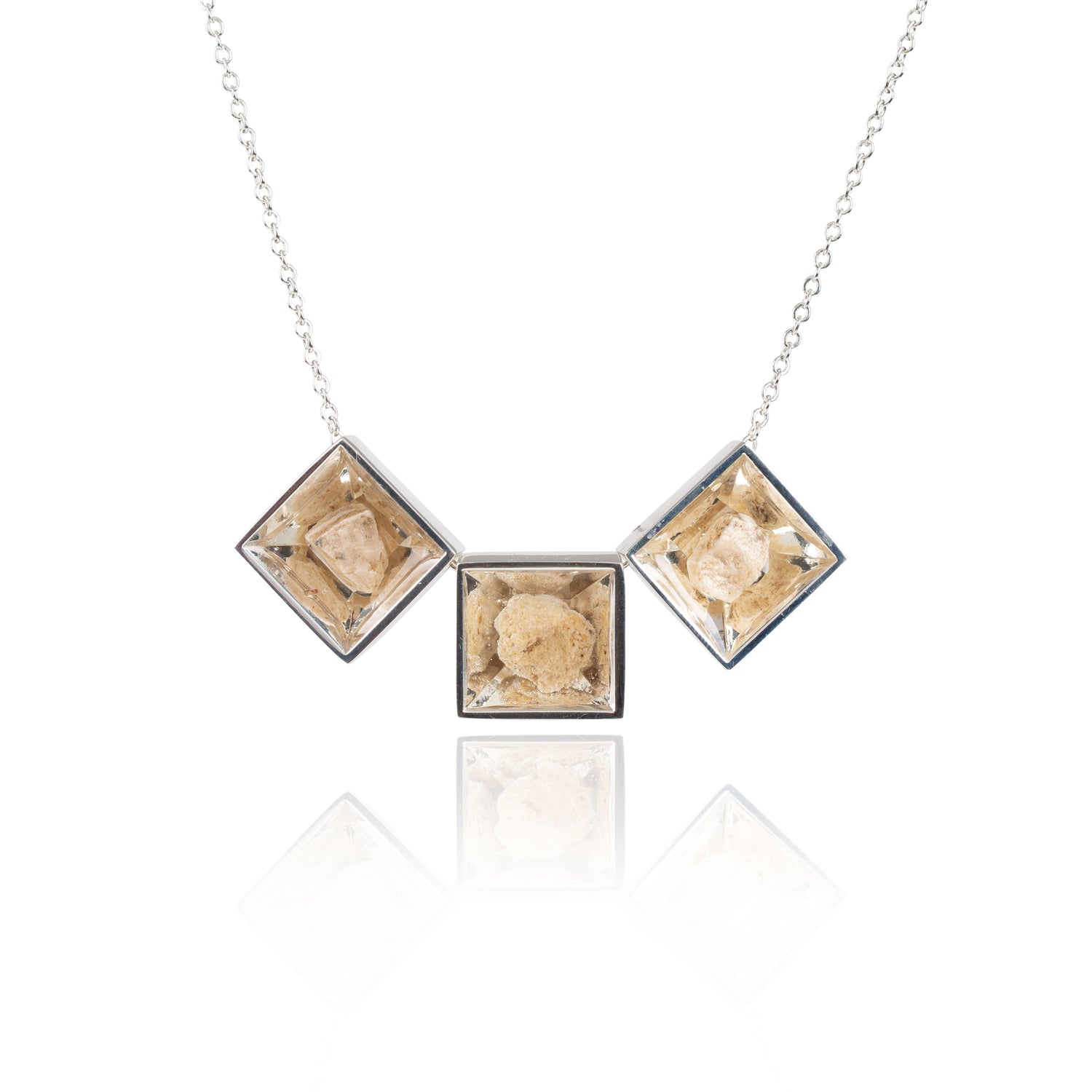 Three small natural tan stones sit in the middle of three separate square shaped metal pendants in a silver color. The pendants are hanging on a silver chain.