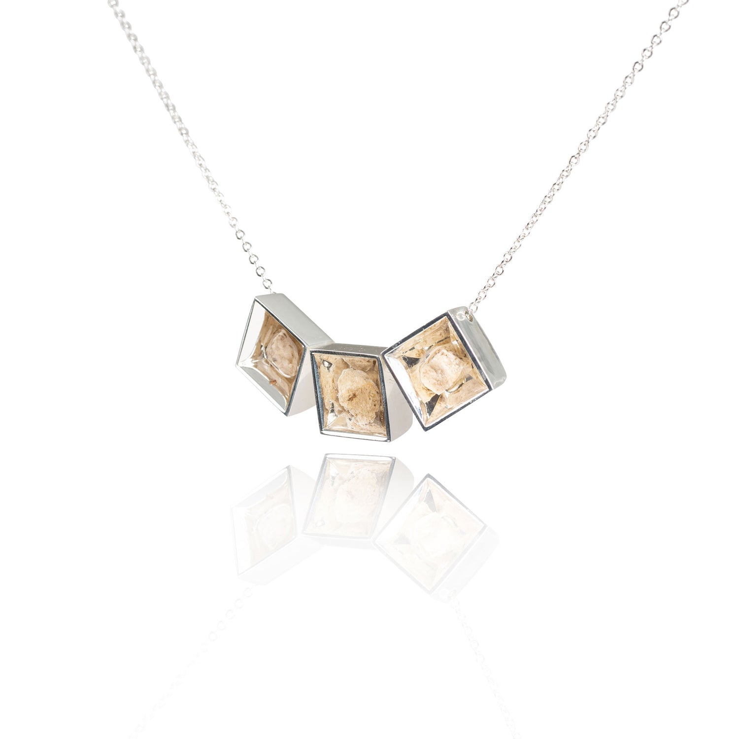 A side view of three small natural tan stones sitting in the middle of three separate square shaped metal pendants in a silver color. The pendants are hanging on a silver chain.